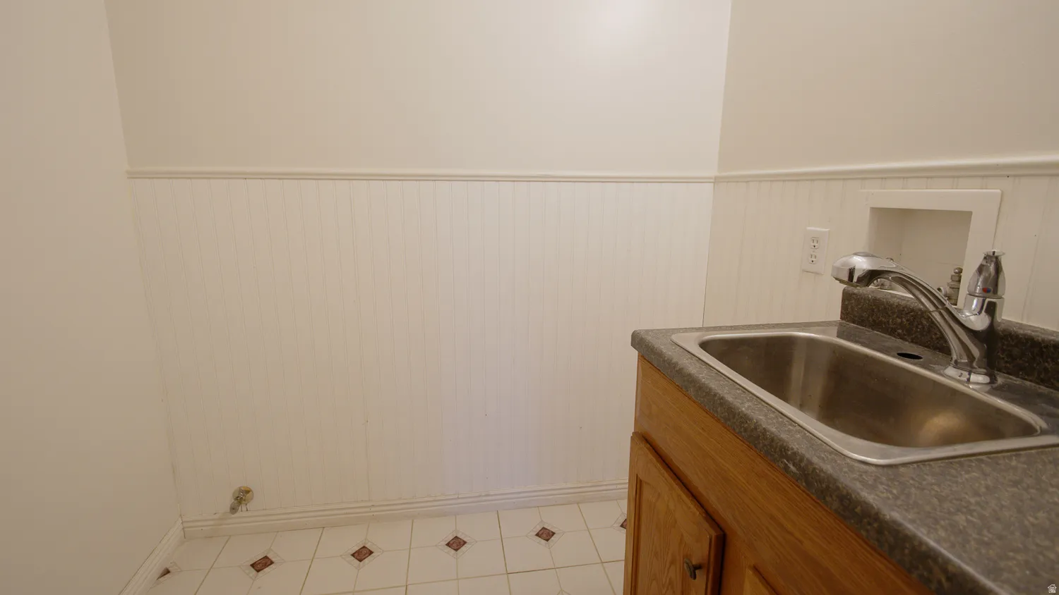 Utility sink with chrome faucet, wood-finish cabinetry, and a dark speckled countertop
