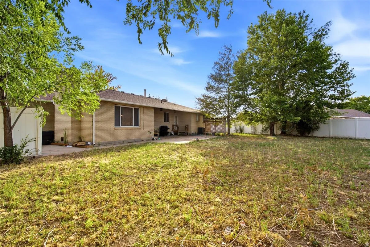 Expansive backyard with a large tree, a white privacy fence, and a concrete patio