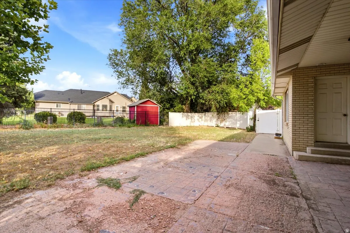 Spacious backyard with mature shade trees, brick paver patio, and detached storage shed