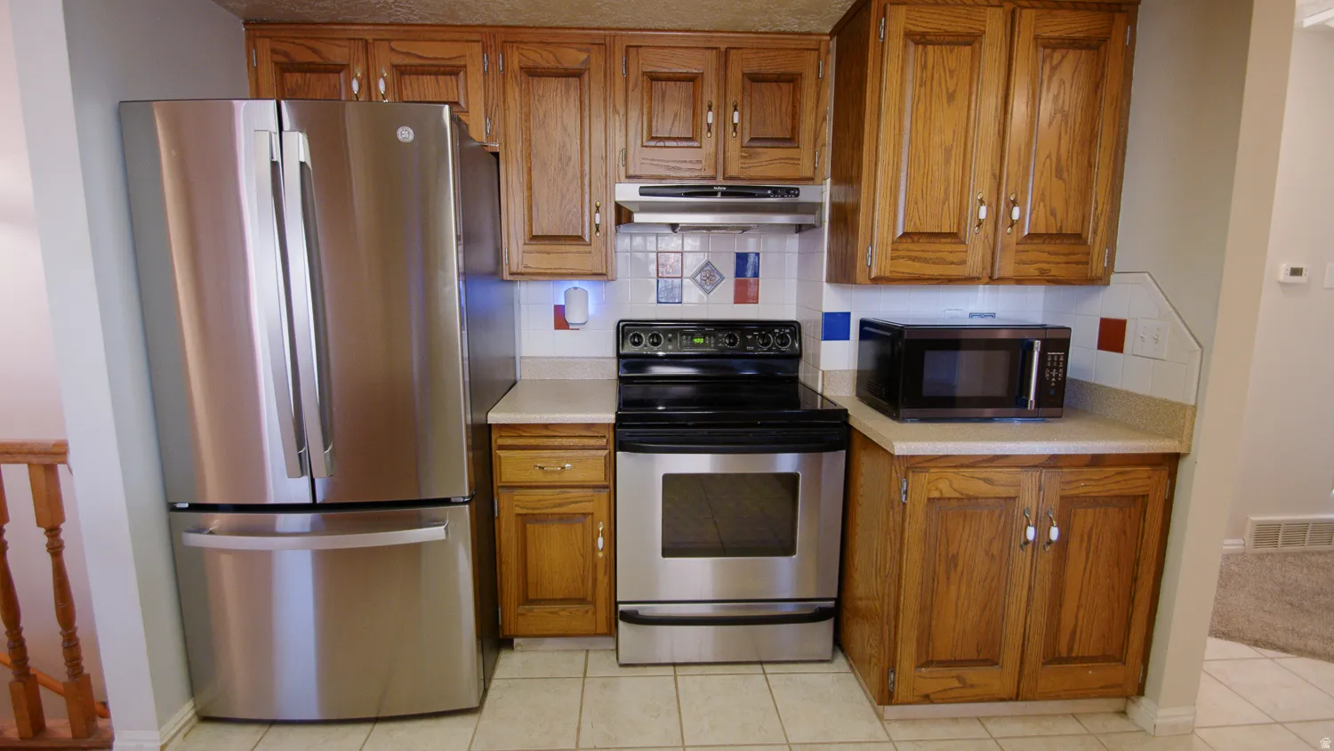 Efficient kitchen featuring wood-finish cabinetry, stainless steel appliances including a French-door refrigerator and electric range, and tile flooring throughout