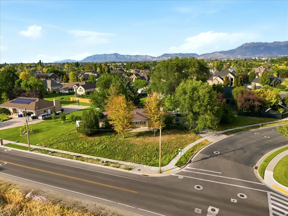 Aerial view showcasing this residential property situated on a corner lot with mature landscaping, manicured lawn, and newly paved streets