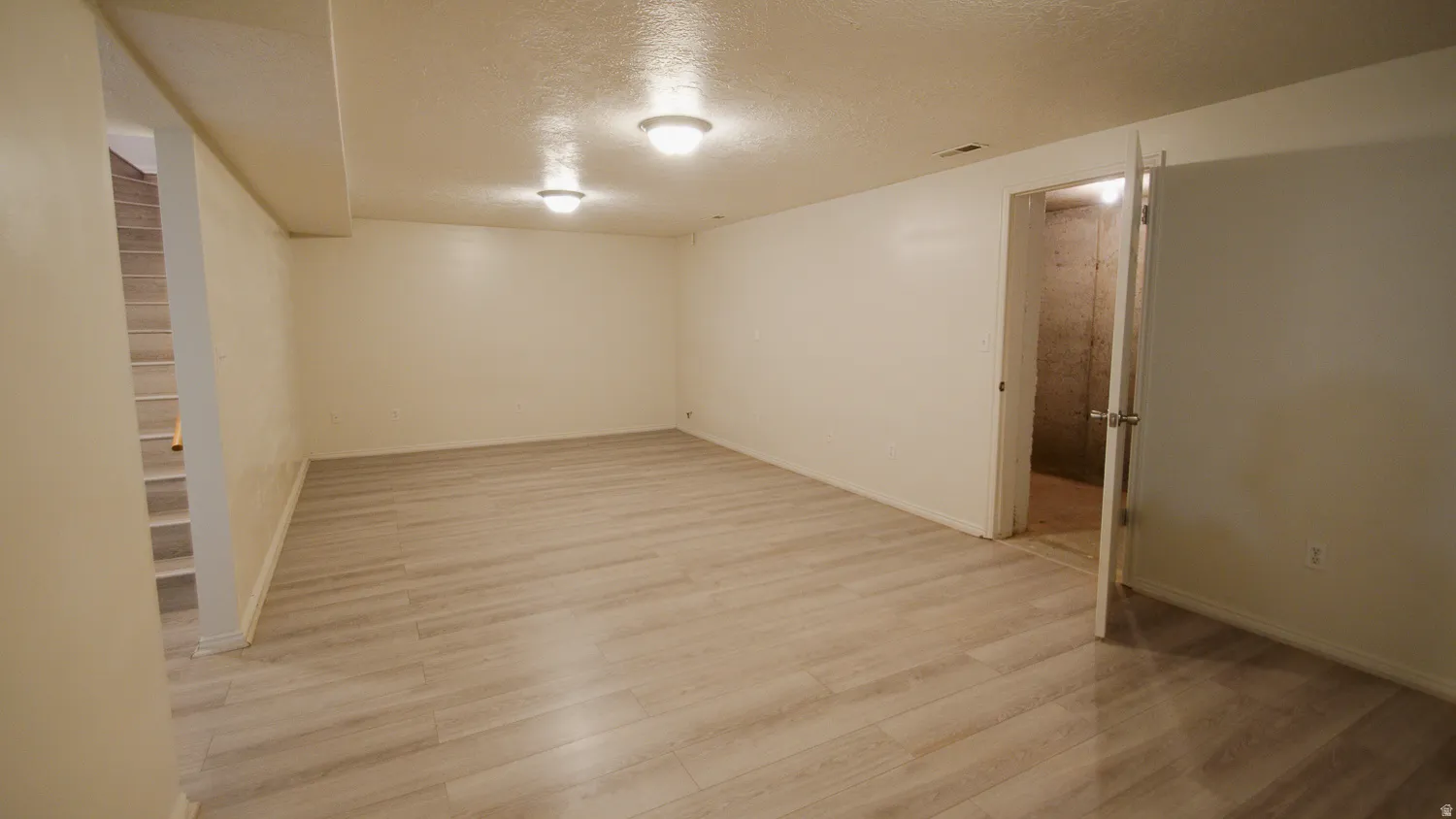 Spacious room featuring light-toned wood-finish flooring, white walls, and flush-mount ceiling lighting