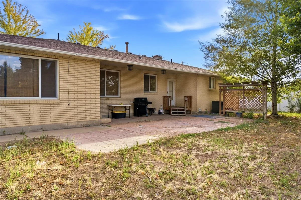 Expansive brick patio with mature shade trees and open lawn space, complemented by a single-story brick exterior featuring multiple windows and a covered entryway with railings