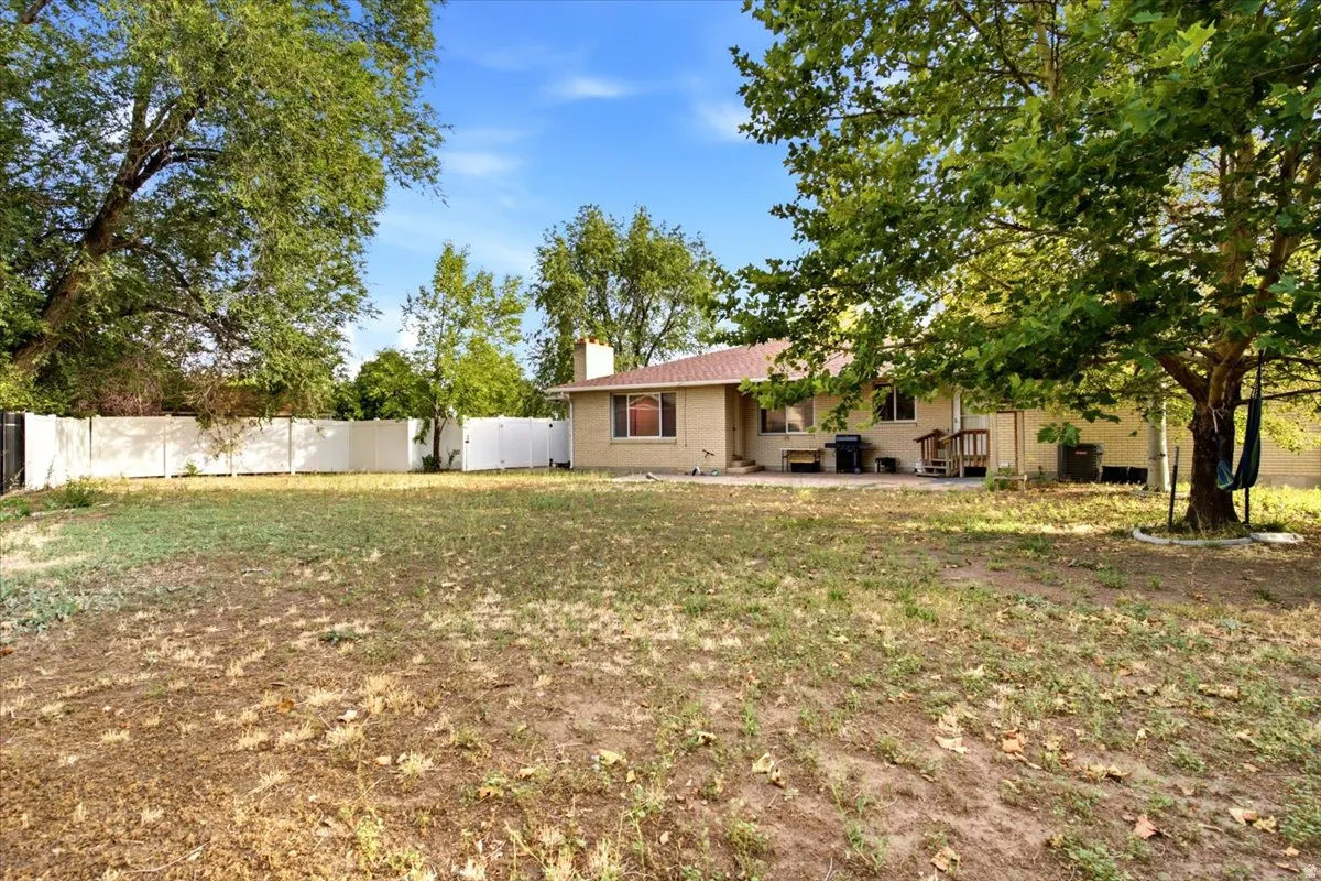 Spacious grounds featuring mature trees and open lawn area, single-story residence with brick exterior and covered porch, detached outbuilding, and fenced perimeter