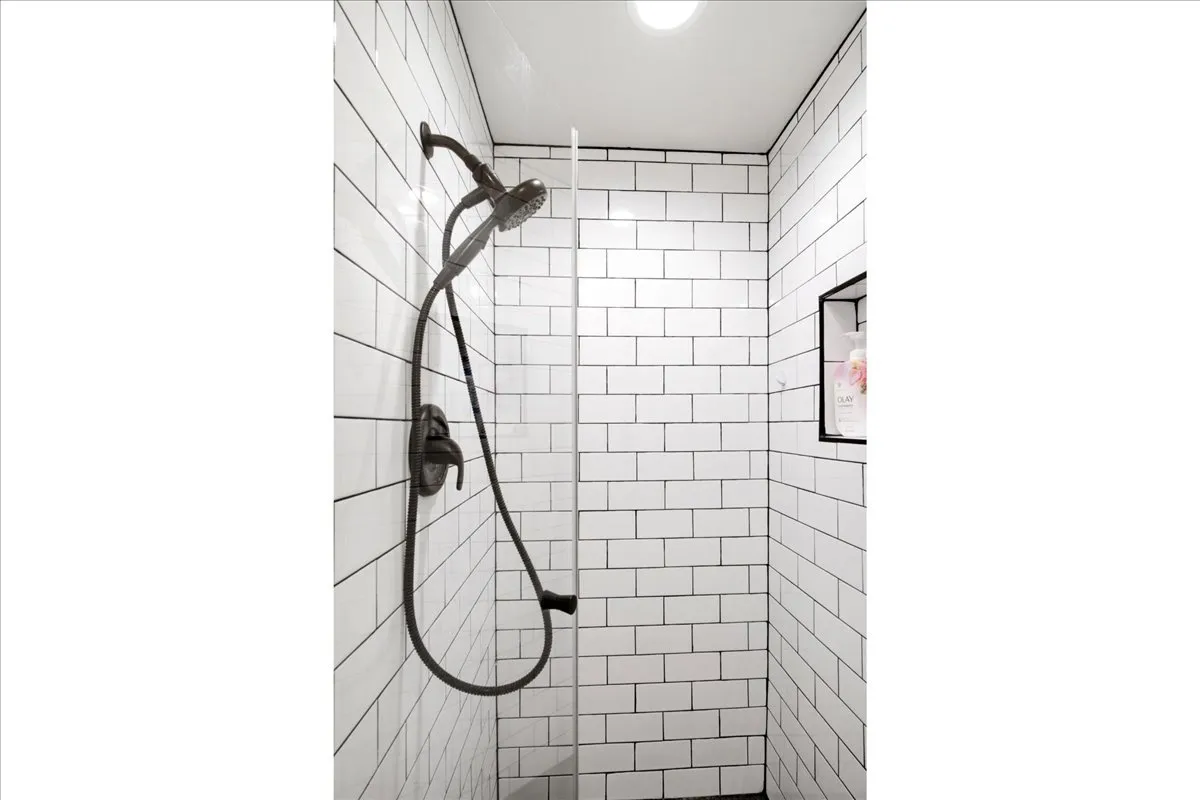 Contemporary shower featuring subway tile walls, dual showerheads with integrated handheld sprayer, matte black fixtures, and recessed ceiling lighting