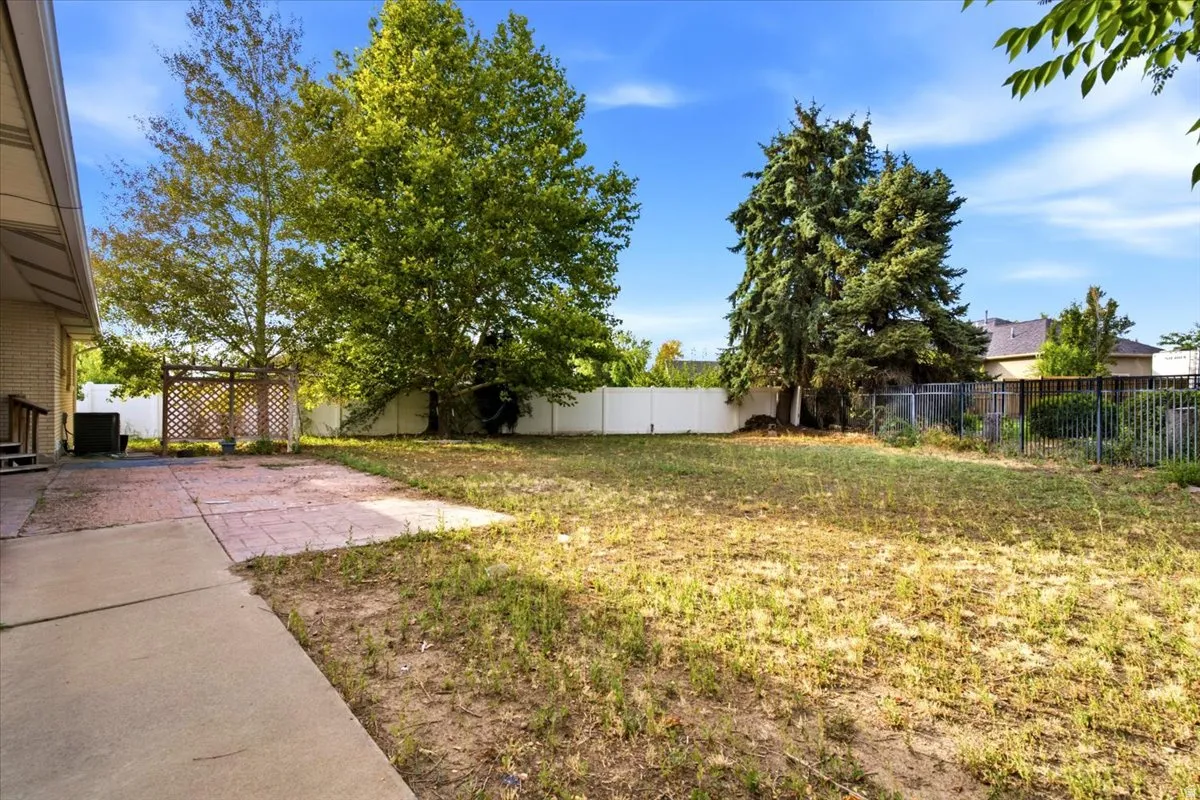 Spacious backyard with mature trees, concrete patio, and fenced perimeter