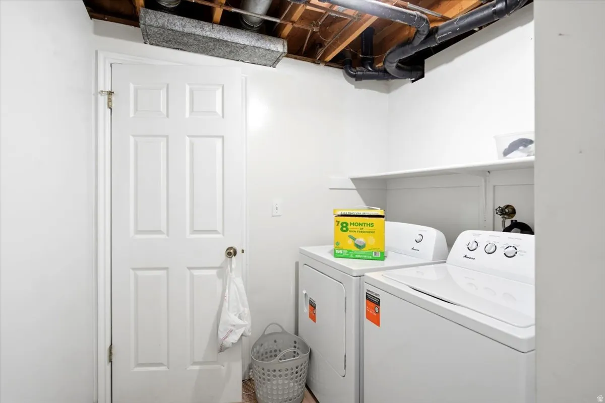 Dedicated laundry room featuring full-size front-load washer and electric dryer with convenient upper shelving for storage, white six-panel entry door, and neutral wall finishes
