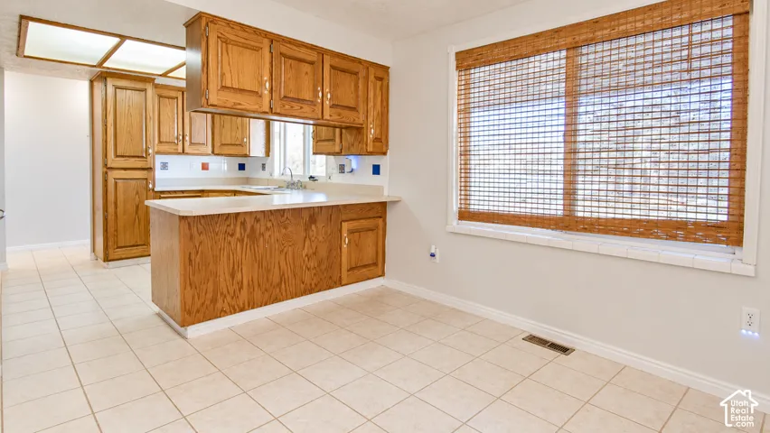 Light-colored tile flooring, wood-finish cabinetry, white countertops, and a built-in window with natural fiber shades