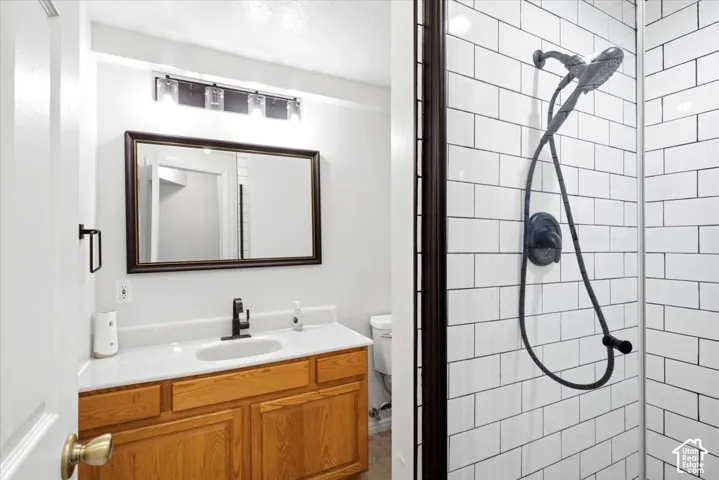 Modern primary bathroom featuring a wood-finish vanity with dual sinks, framed mirror with integrated lighting, and subway tile shower enclosure with rainfall showerhead and handheld spray fixture