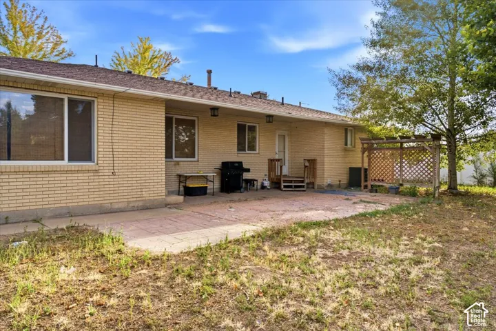 Expansive brick patio with mature shade trees and open lawn space, complemented by a single-story brick exterior featuring multiple windows and a covered entryway with railings