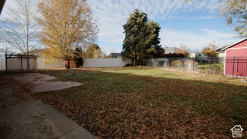 Expansive fenced yard with mature trees, established lawn, concrete patio, and a dedicated storage shed