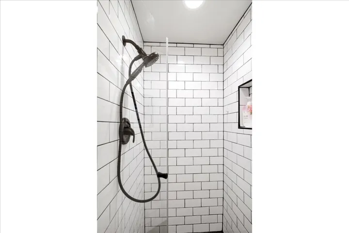 Contemporary shower featuring subway tile walls, dual showerheads with integrated handheld sprayer, matte black fixtures, and recessed ceiling lighting