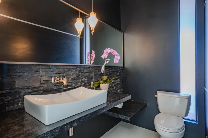 Modern powder room featuring a vessel sink, wall-mounted faucet, and stacked stone accent wall
