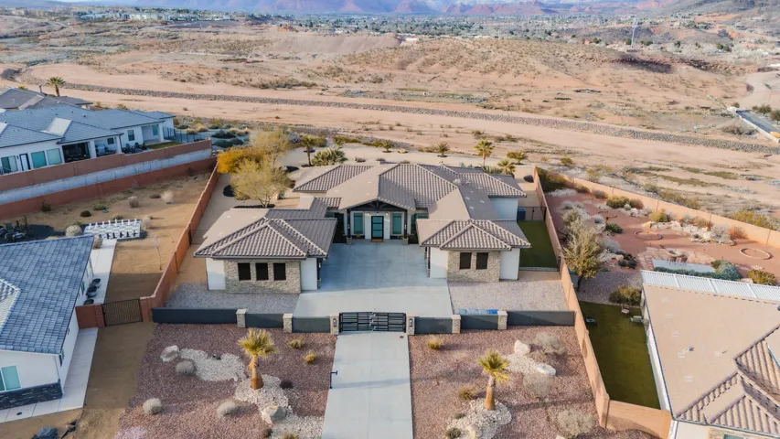 Desert landscape featuring a single-story residence with a tiled roof, stone accents, a paved driveway, and an enclosed front courtyard with a gate