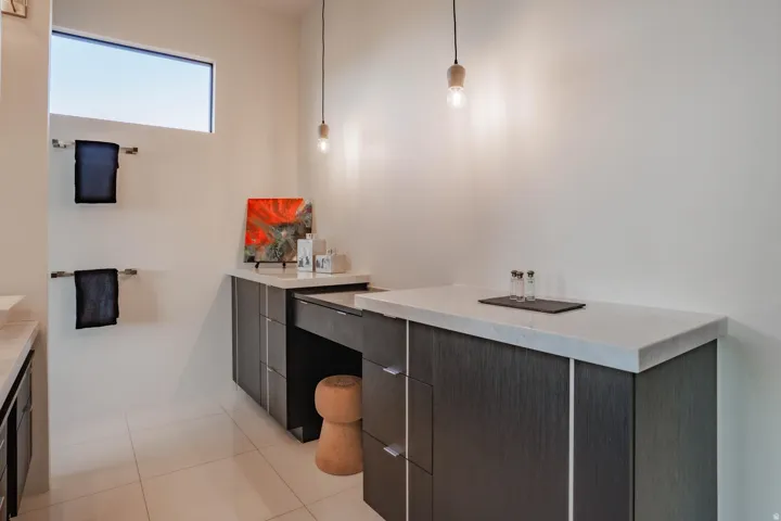 White tile flooring, elongated transom window, dark wood-finish cabinetry, light-colored countertops, and pendant lighting fixtures