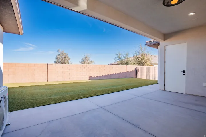 Covered patio with concrete flooring, artificial turf, and block wall fencing