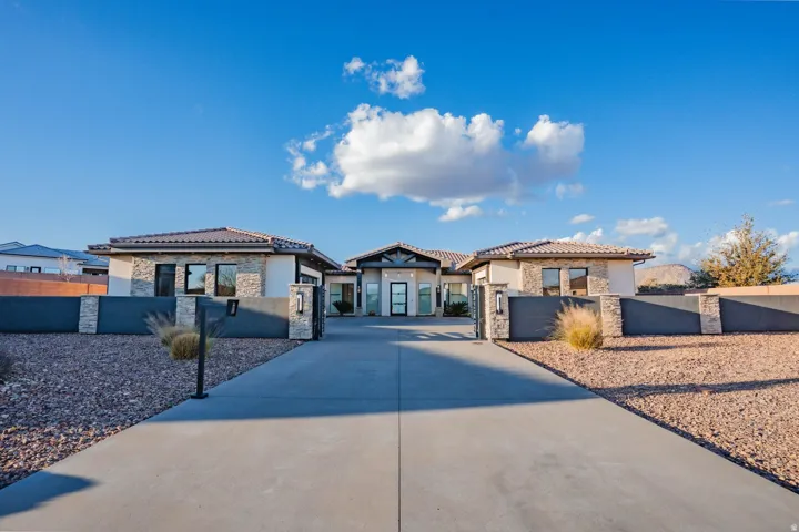 Expansive driveway leading to a stone facade residence with a tile roof, decorative stone pillars, and a modern entry door