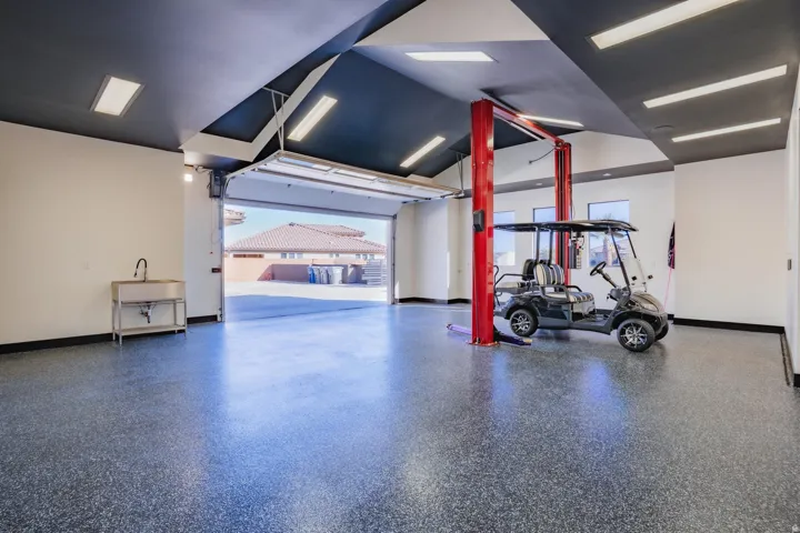 Spacious garage with an epoxy floor finish, vehicle lift, stainless steel utility sink, and recessed lighting