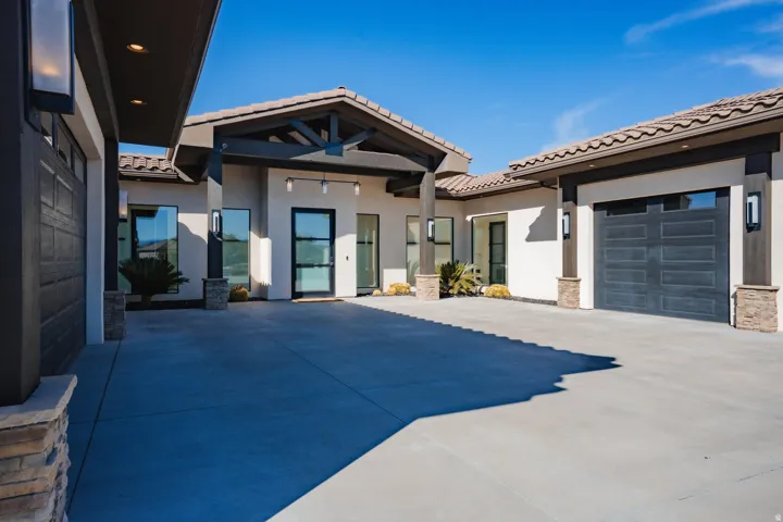 Contemporary exterior featuring a smooth stucco finish, stone-clad architectural columns, a tiled roof, and a dark-paneled garage door