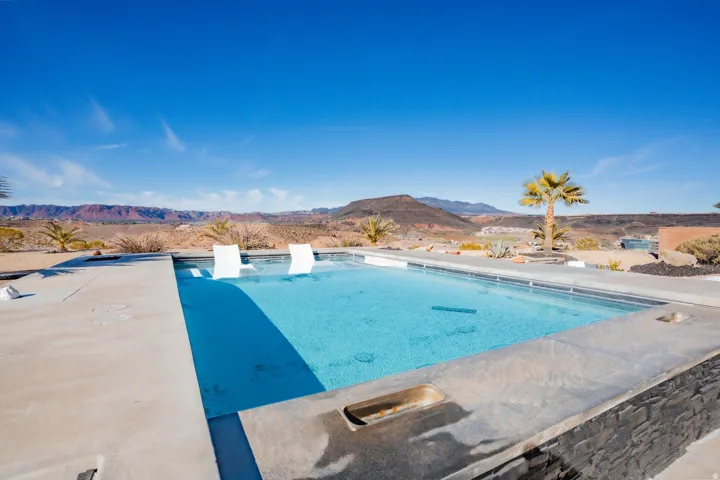 In-ground pool featuring a concrete surround, dark stone-finish accent wall, and integrated seating