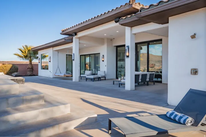 Expansive concrete patio with multiple sliding glass doors, exterior wall sconces, and a covered outdoor living area