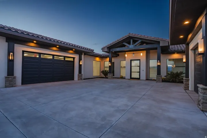 Expansive concrete driveway, attached garage with frosted glass panels, wood beam entry, and stucco exterior with stone accents