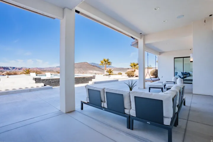 Expansive concrete patio with a covered outdoor living area, featuring a built-in spa, a suspended swing, and an exterior glass sliding door
