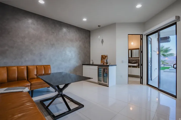 Polished tile flooring, accent wall with textured finish, built-in wet bar with beverage cooler, recessed lighting, and sliding glass doors