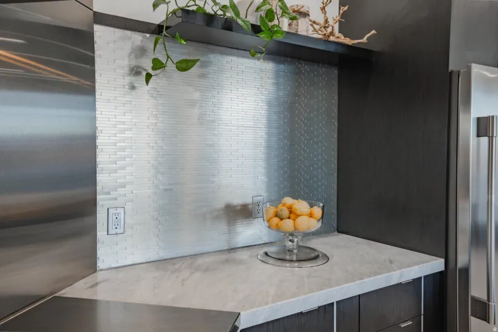 Stainless steel appliances, light-toned countertop, dark wood-finish cabinetry, and a textured backsplash