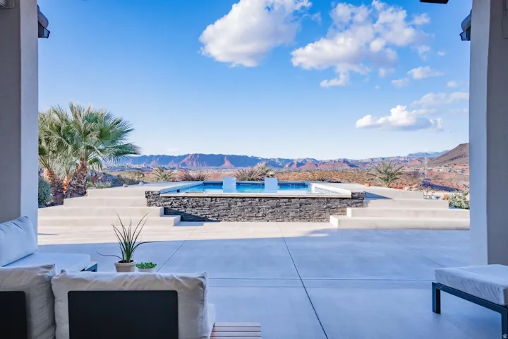 Expansive outdoor patio with concrete flooring, tiered steps, an in-ground pool featuring a stone-clad surround, and distant mountain scenery