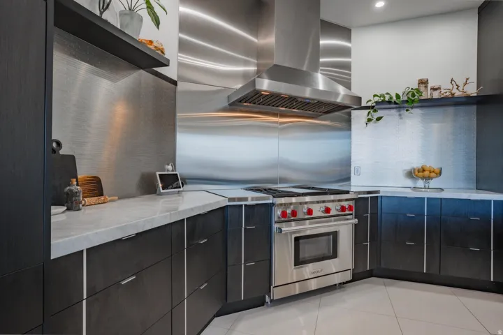 Contemporary kitchen featuring stainless steel professional-grade appliances, including a six-burner range with matching hood, soft-close cabinetry in matte black finish, quartz countertops, and a mirrored backsplash