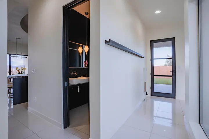 White tile flooring with a glossy finish, black framed glass door, recessed lighting, and a powder room with a vessel sink and pendant lighting