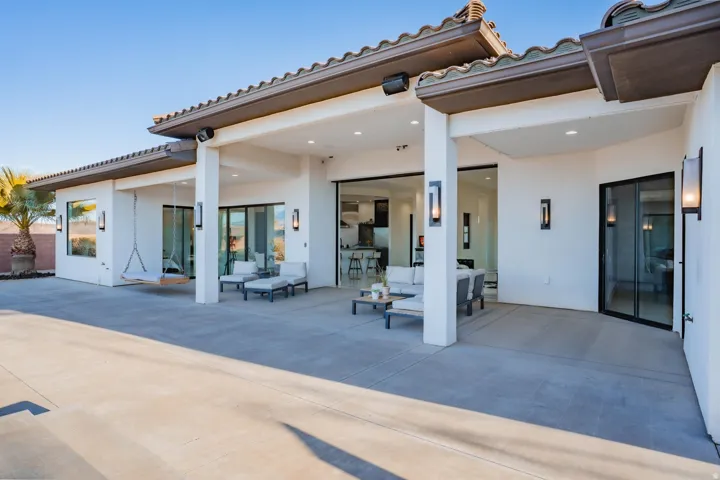 Expansive concrete patio with a covered outdoor living area, featuring recessed lighting and multiple sliding glass doors