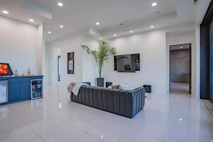 Bright open-concept living space with large format tile flooring, recessed lighting, and a built-in wet bar featuring an under-counter refrigerator