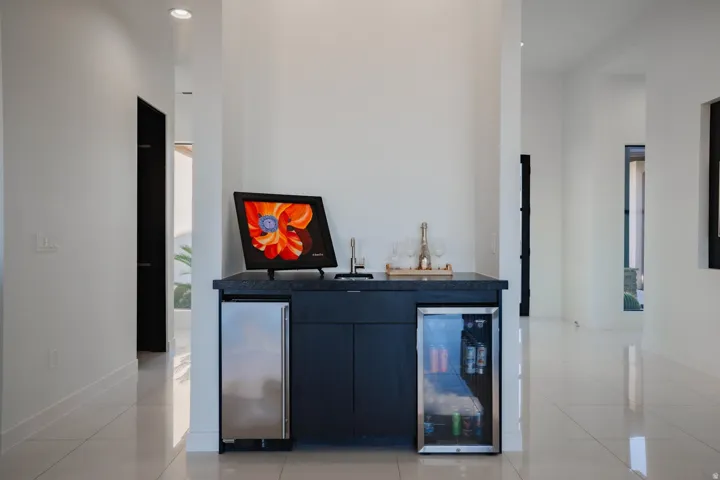 Built-in bar with dark cabinetry, integrated beverage refrigerator, under-counter ice maker, and dark countertop