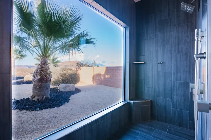 Full-height window, dark large-format tile walls, tile flooring, built-in tile bench, and rainfall showerhead with handheld sprayer