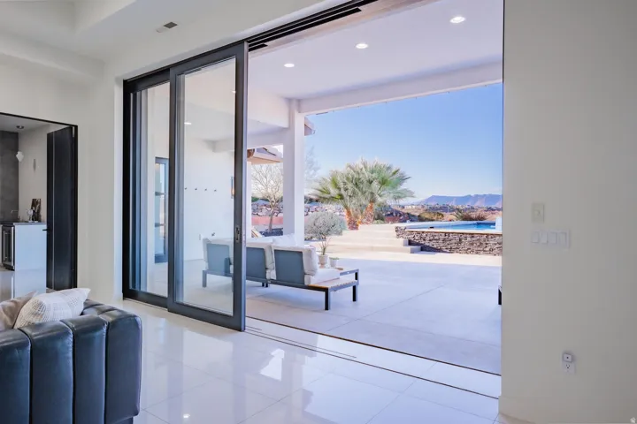 Expansive sliding glass doors opening to an outdoor patio with a pool, concrete decking, and stone wall features