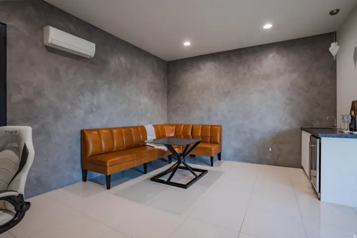 White tile flooring, textured gray wall finish, recessed lighting, built-in wet bar with under-counter refrigerator, and wall-mounted climate control unit