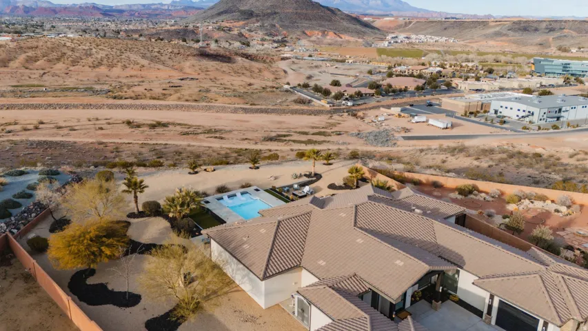 Aerial perspective showcasing a sprawling property featuring a rectangular swimming pool, mature desert landscaping, and tiled roofing