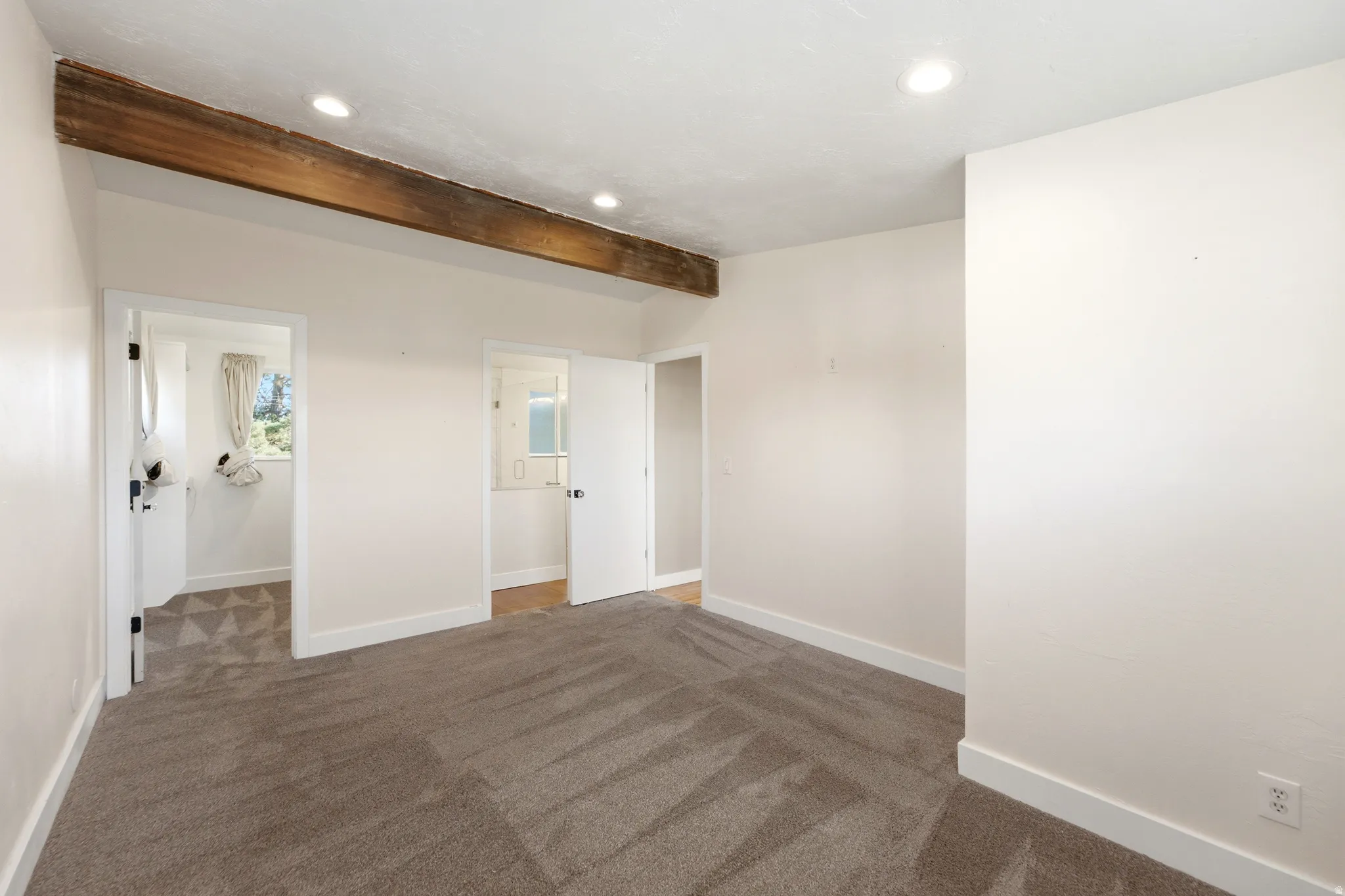 Recessed lighting, wood beam accents, light neutral walls, and grey patterned carpeting