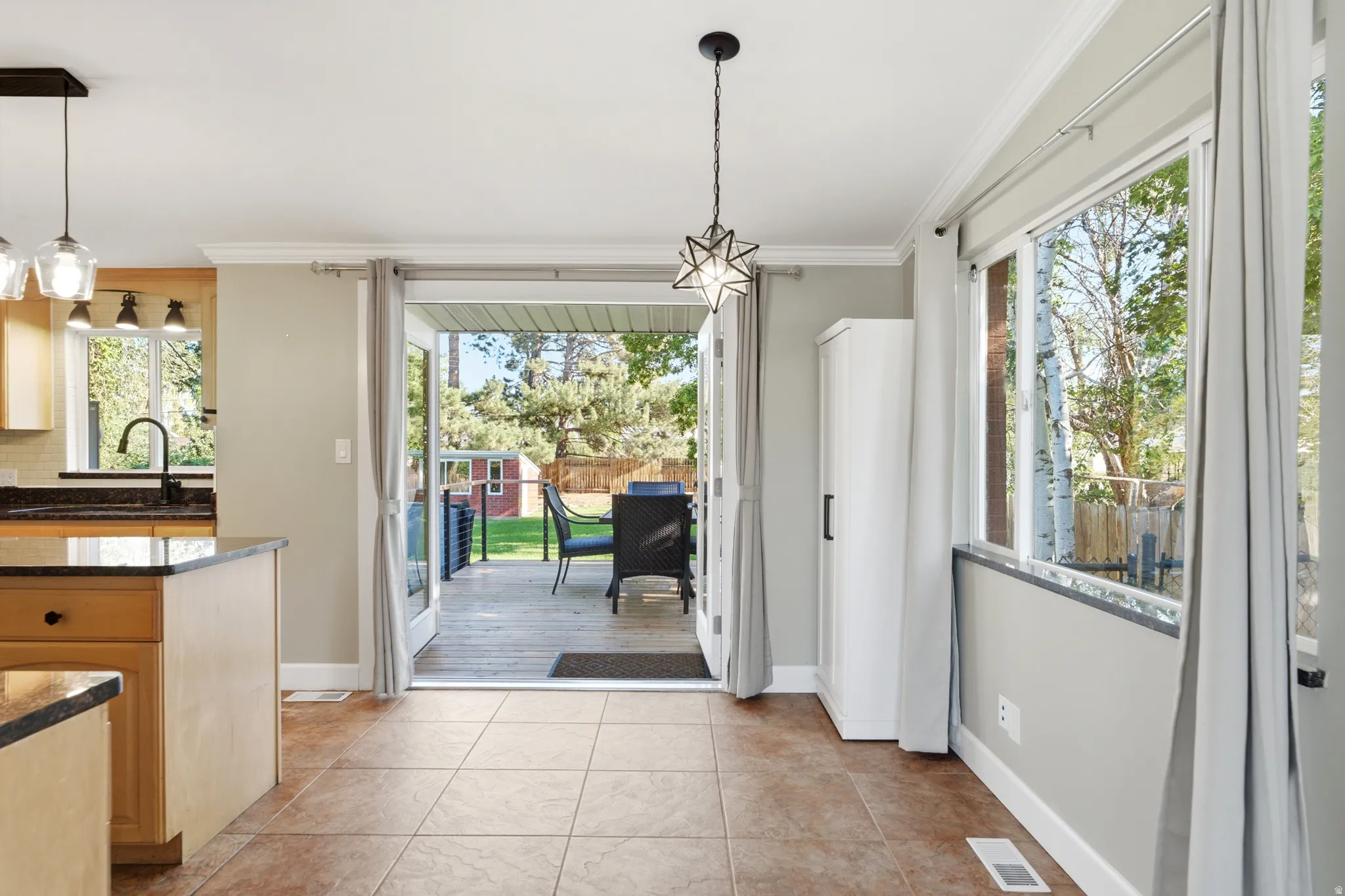 Tile flooring, patio access, kitchen island with dark countertop, large windows, crown molding