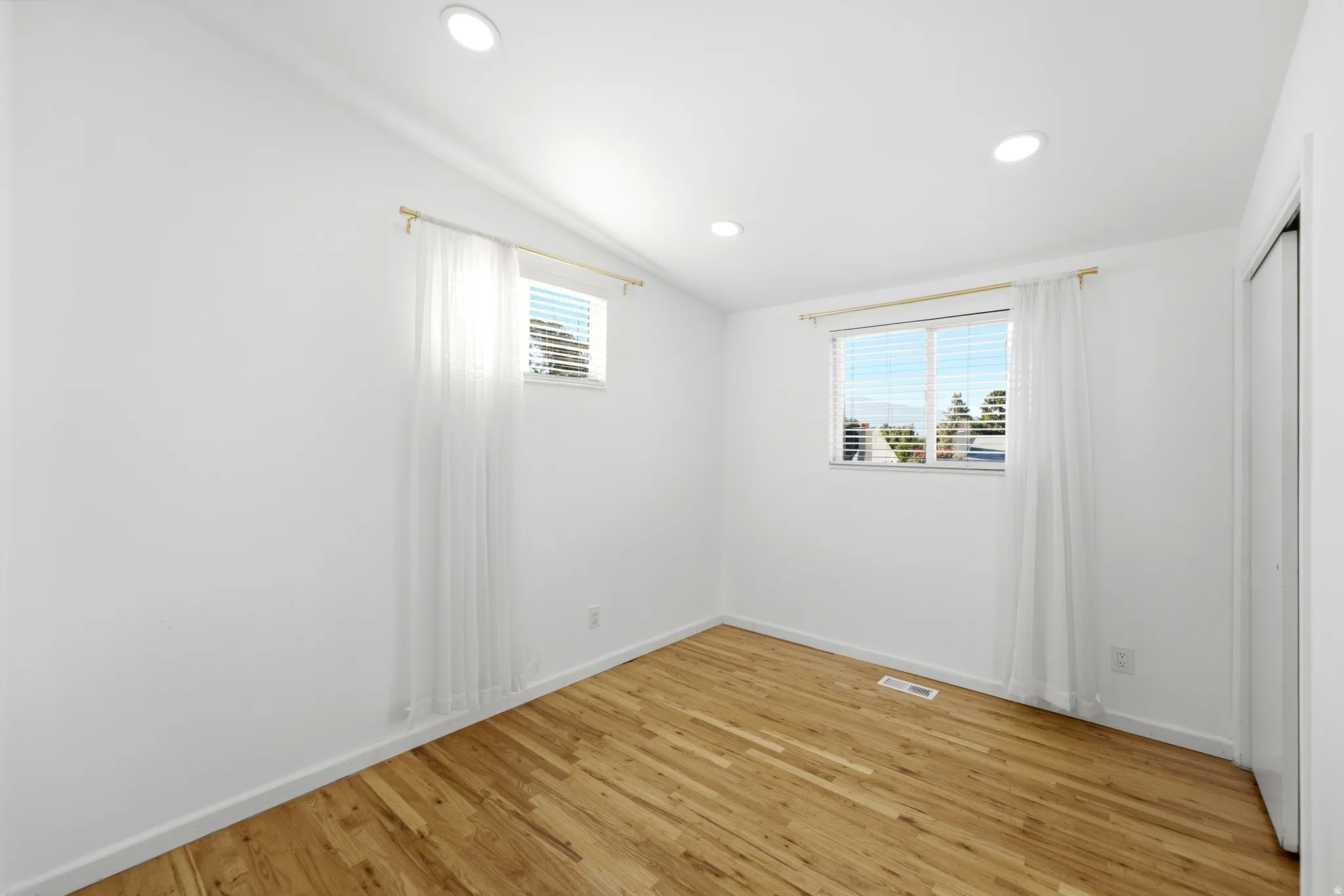 Recessed lighting, wood-finish flooring, two windows with blinds, and white walls