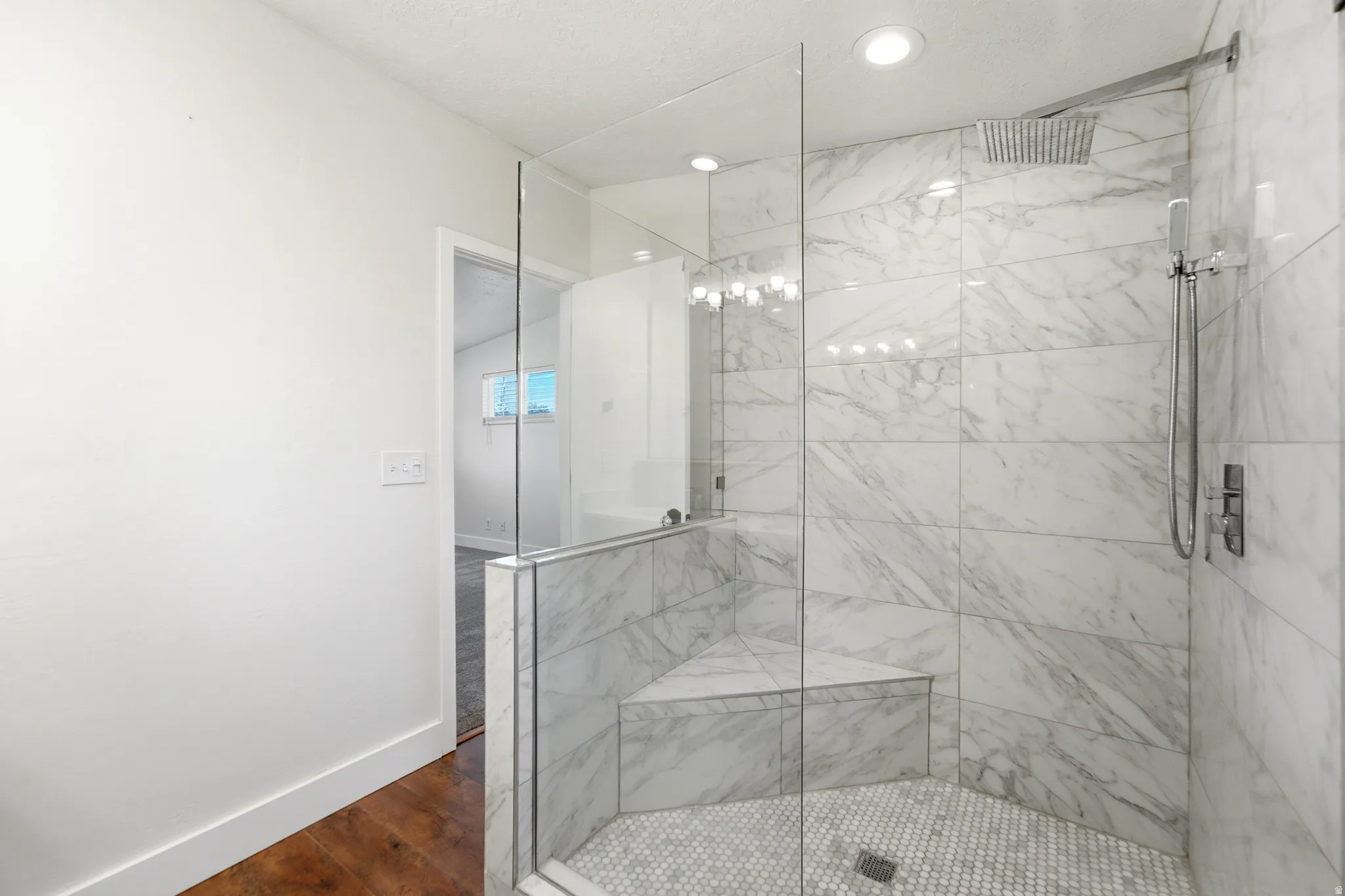Glass-enclosed shower featuring large format tile walls, a built-in bench, and a rain showerhead