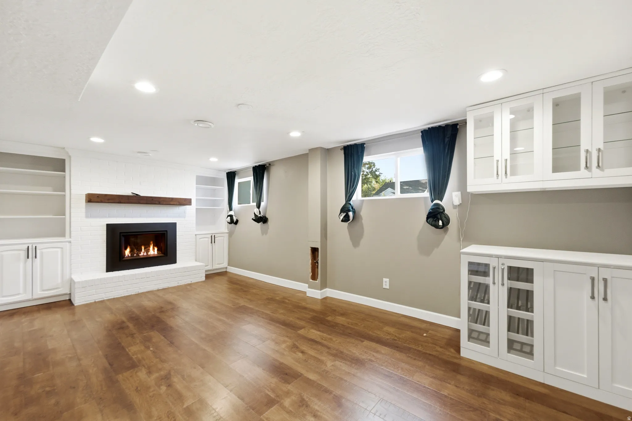 Wood-finish flooring, recessed lighting, and a white brick fireplace with a wood mantel