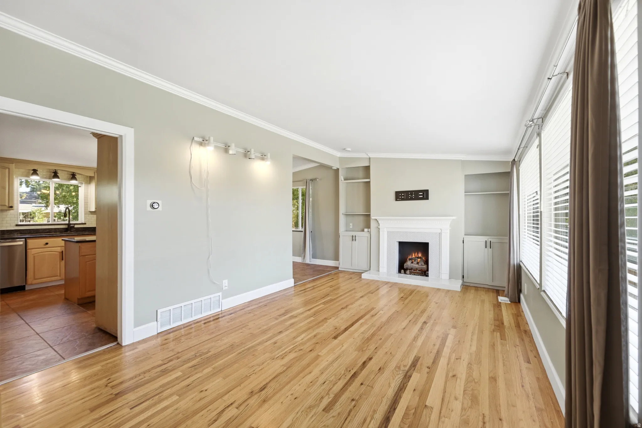 Hardwood flooring throughout, fireplace with mantle and built-in shelving, white crown molding, and large windows with blinds