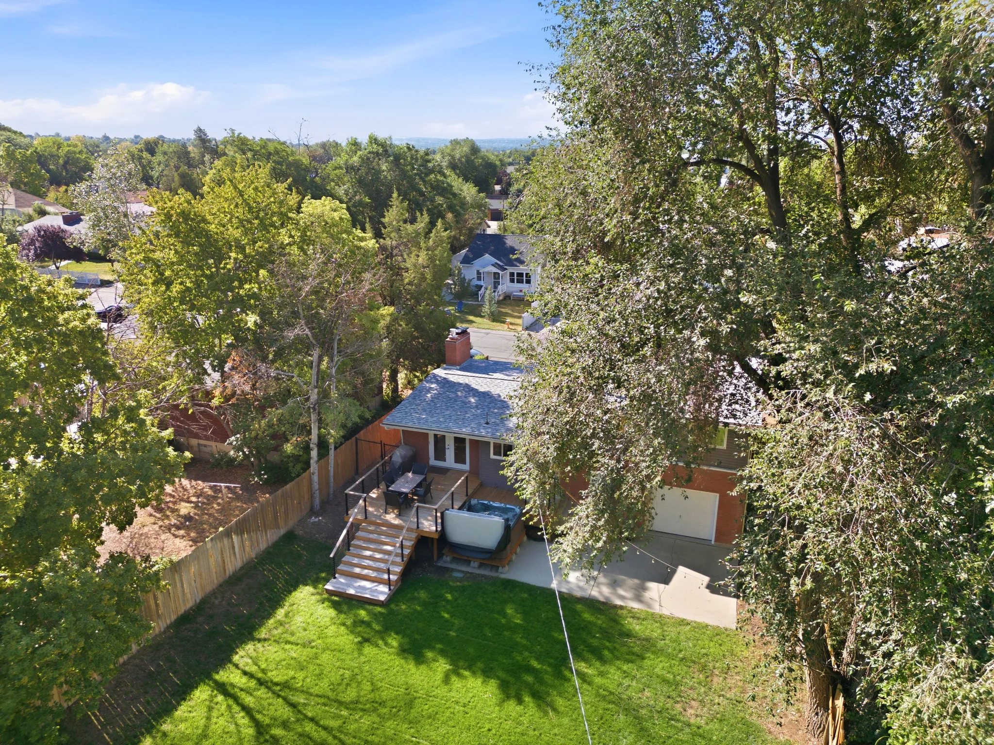 Expansive green lawn, multi-level wood deck, outdoor hot tub, wood privacy fencing, and mature trees