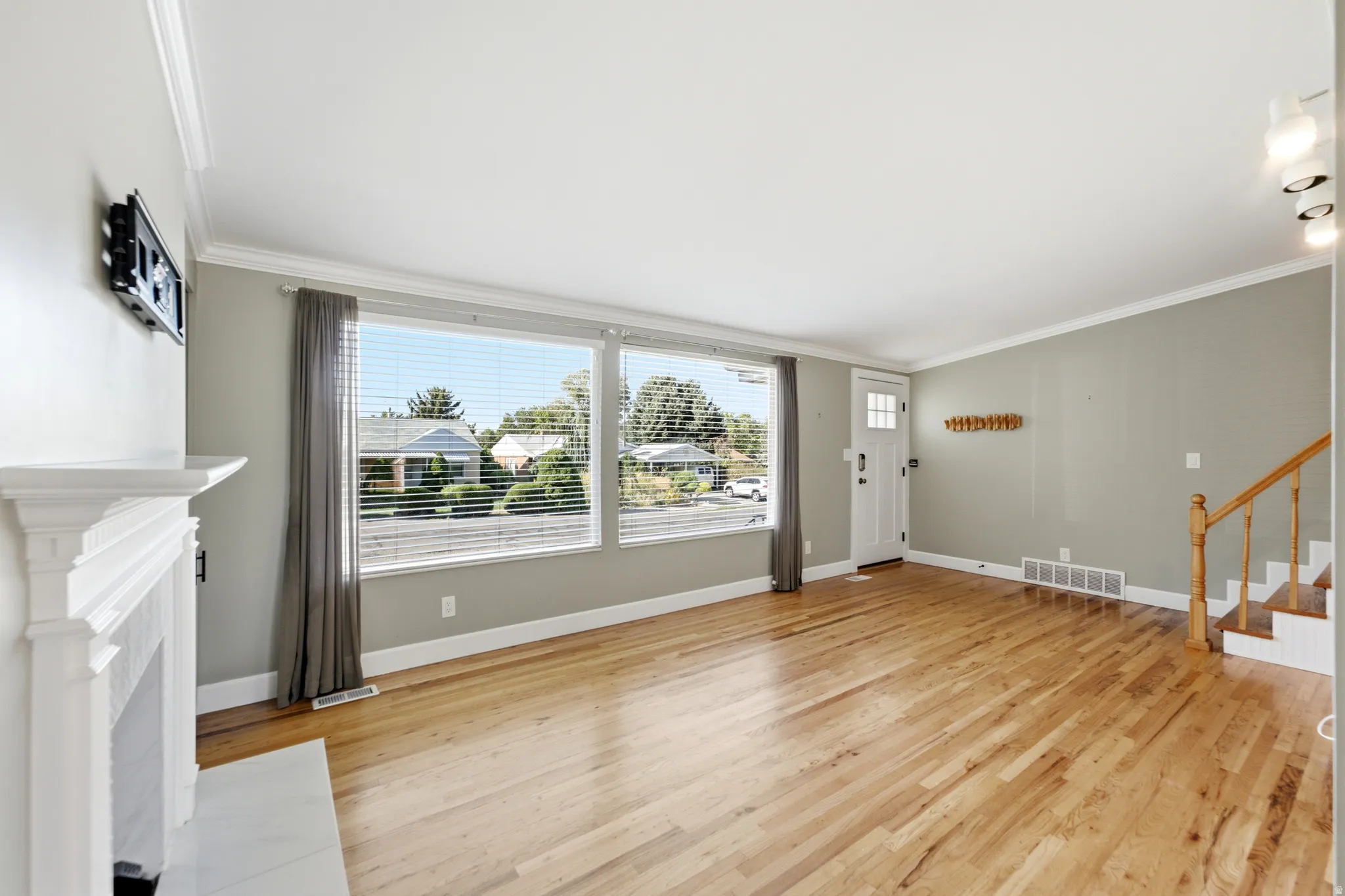 Hardwood-finish flooring throughout, bright white trim and crown molding, and a traditional fireplace with a white mantel and hearth