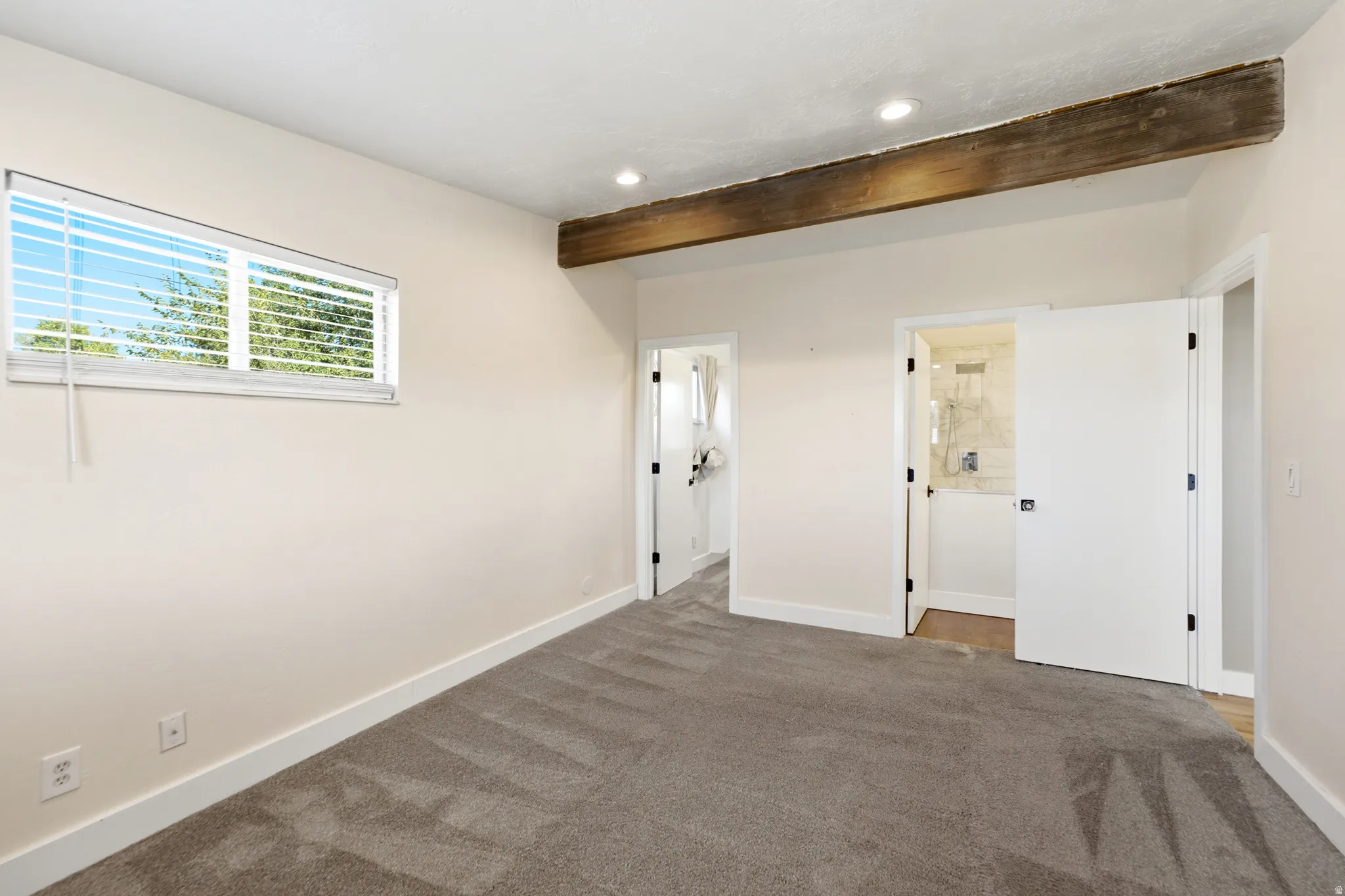 Plush carpeting, horizontal window with blinds, recessed ceiling lighting, exposed wood beam, and white interior doors