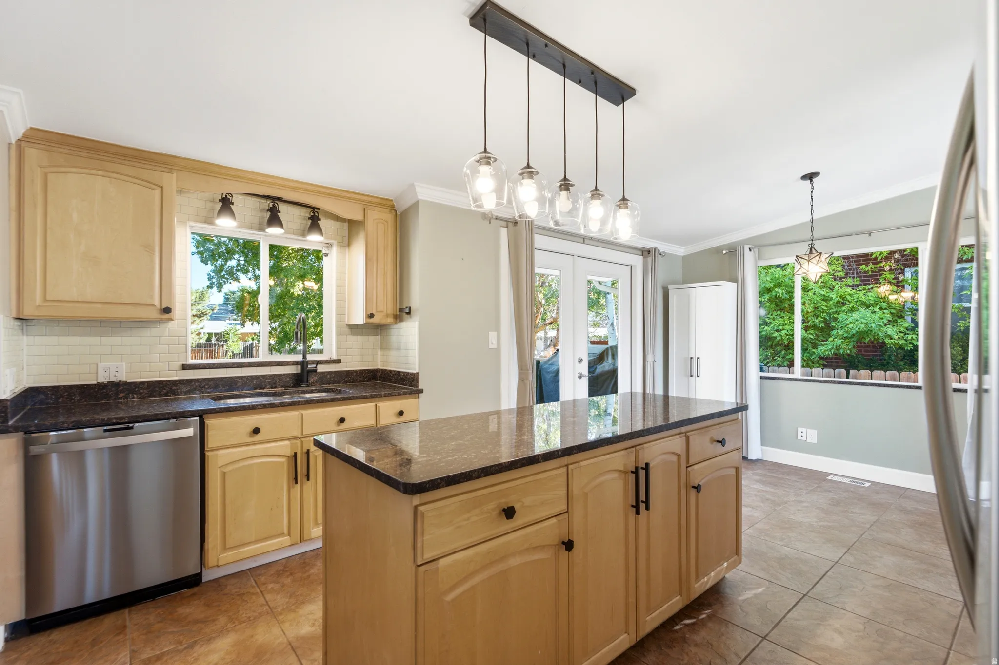 Kitchen featuring wood cabinetry, dark countertops, a stainless steel dishwasher, and a center island with pendant lighting