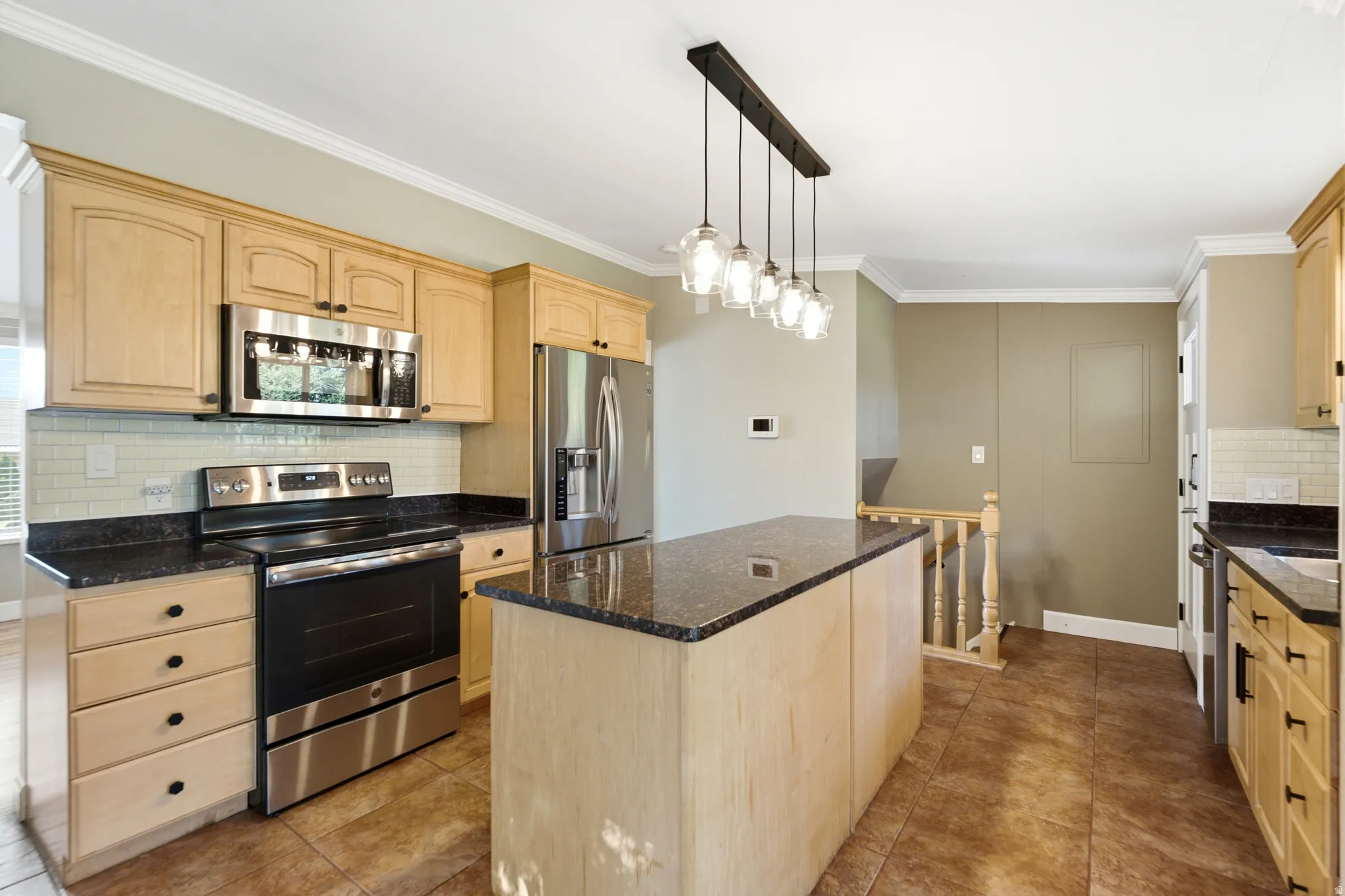Kitchen featuring wood-finish cabinetry, stainless steel appliances, dark stone countertops, a tile backsplash, and a central island with pendant lighting